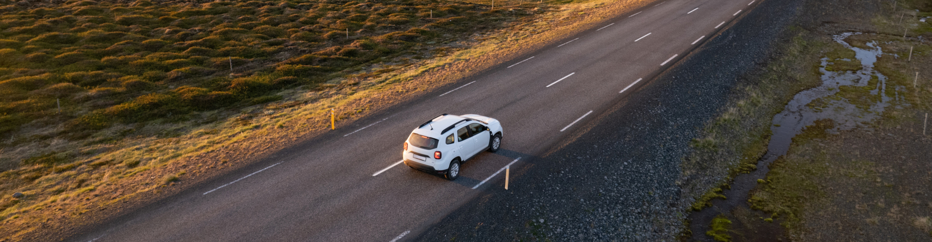 Aerial view of a white car driving along a winding road surrounded by greenery.